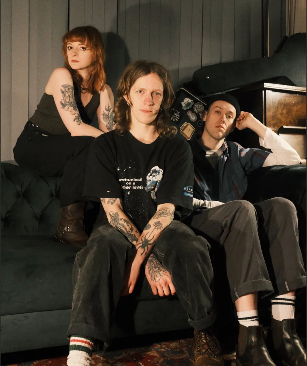 The three members of the band on a green velvet sofa
